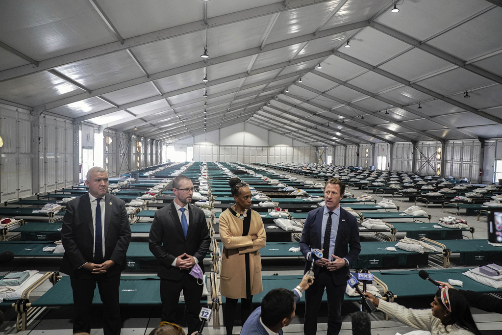 New York's Office of Immigrant Affairs Commissioner Manuel Castro, far left, Health and Hospital Vice President Dr. Ted Long, second from left, Deputy Mayor for Health and Human Services Anne Williams-Isom, second from right, and Emergency Management Commissioner Zach Iscol, far right, hold a news briefing in the sleeping area of the city's latest temporary shelter on Randalls Island, Oct. 18, 2022, in New York. New York Mayor Eric Adams announced a plan Monday, Aug. 7, 2023, to house as many as 2,000 migrants on Randalls Island, in the East River, where a migrant center was set up in 2022 and then taken down weeks later. (AP Photo/Bebeto Matthews, File)