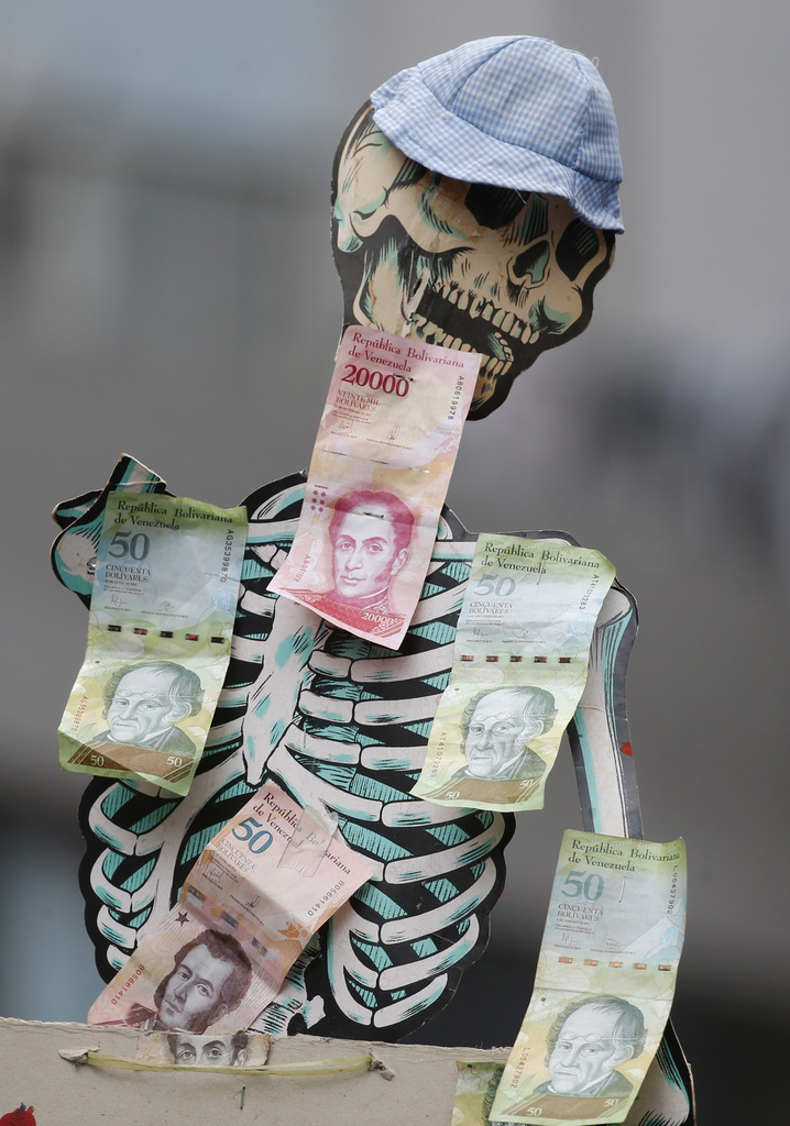 FILE - A skeleton is adorned with Venezuelan Bolivar bills to draw attention to the devaluation of the currency and hunger, during an opposition march in Caracas, Venezuela, March 10, 2020. (AP Photo/Ariana Cubillos, File)