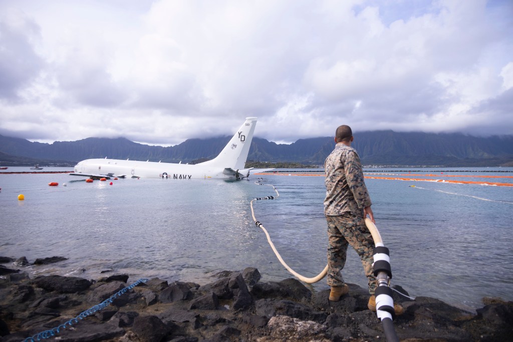 A U.S. Marine holds a fuel hose being secured during defueling operations on a downed U.S. Navy P-8A Poseidon in waters just off the runway at Marine Corps Air Station Kaneohe Bay, Marine Corps Base Hawaii, Nov. 26, 2023. The successful defueling of the downed P-8A was critical to the execution of the aircraft salvage plan. (U.S. Marine Corps photo by Sgt. Brandon Aultman)