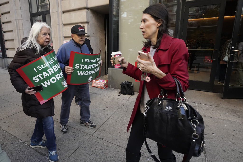 Isabel Johnston, left, and John Papandrea carry signs supporting Starbucks workers outside a Starbucks on New York's Upper West Side, Thursday, Nov. 16, 2023. Thousands of workers at more than 200 U.S. Starbucks stores plan to walk off the job Thursday in what organizers say is the largest strike yet in the two-year-old effort to unionize the company's stores. (AP Photo/Richard Drew)