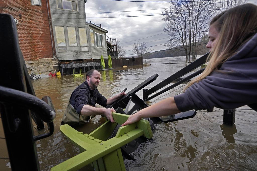 Nathan Sennett hands furniture to Tori Grasse as they work in hip-deep water on the patio of the Quarry Tap Room, Tuesday, Dec. 19, 2023, in Hallowell, Maine. Waters continue to rise in the Kennebec River following Monday's severe storm. (AP Photo/Robert F. Bukaty)
