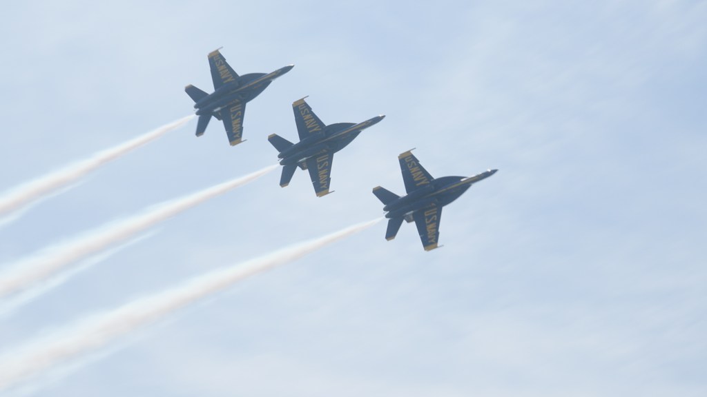 3 Blue Angel jets fly side-by-side in the clear blue sky leaving behind a trail of white smoke. 